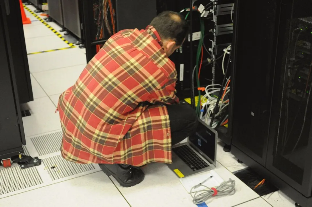 A technician with a laptop works on a server rack in the NERSC data center.