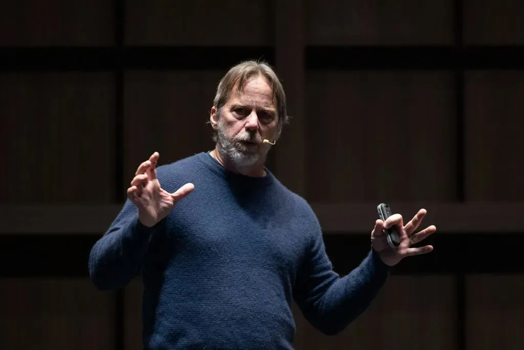 Tenstorrent CEO Jim Keller speaking on stage, gesturing with both hands while holding a phone.
