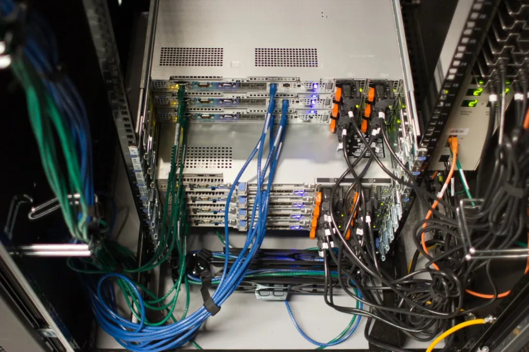 A close-up of rack-mounted servers and network cabling inside a data center, the IT hardware that accounts for most of the cost of new AI capacity.