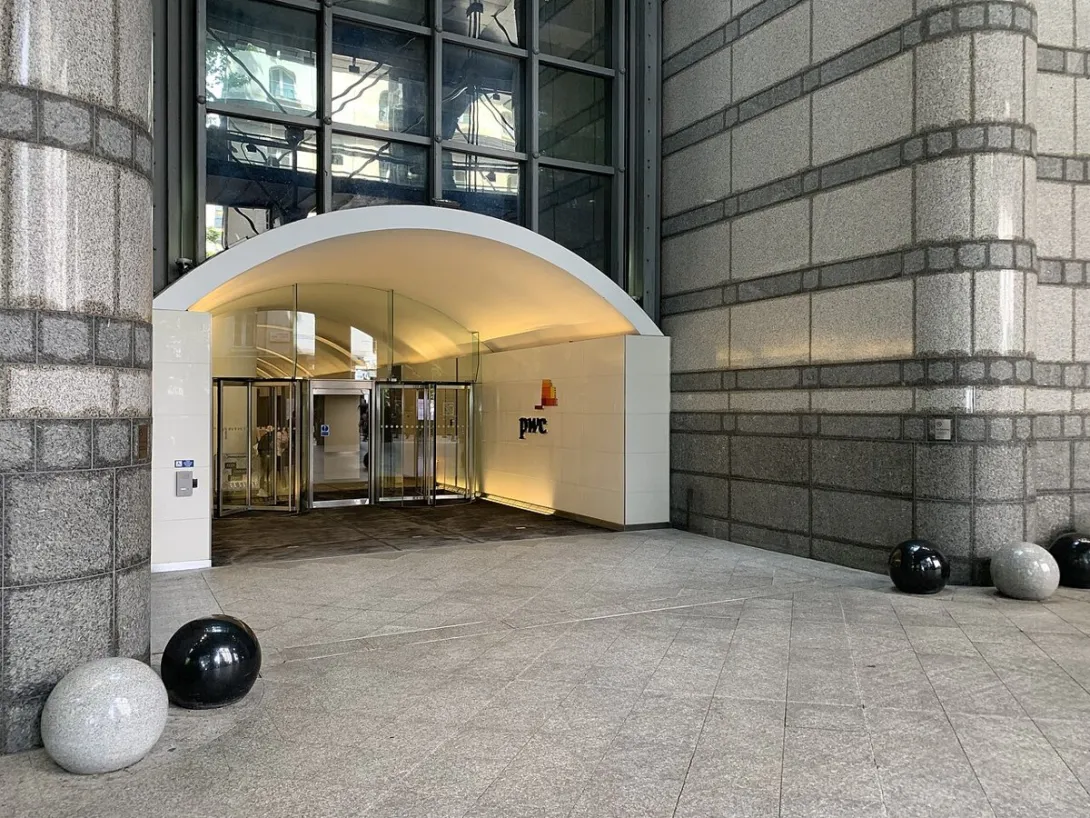 The entrance to PwC offices at 1 Embankment Place in London, with the PwC logo on the wall beside the revolving doors.